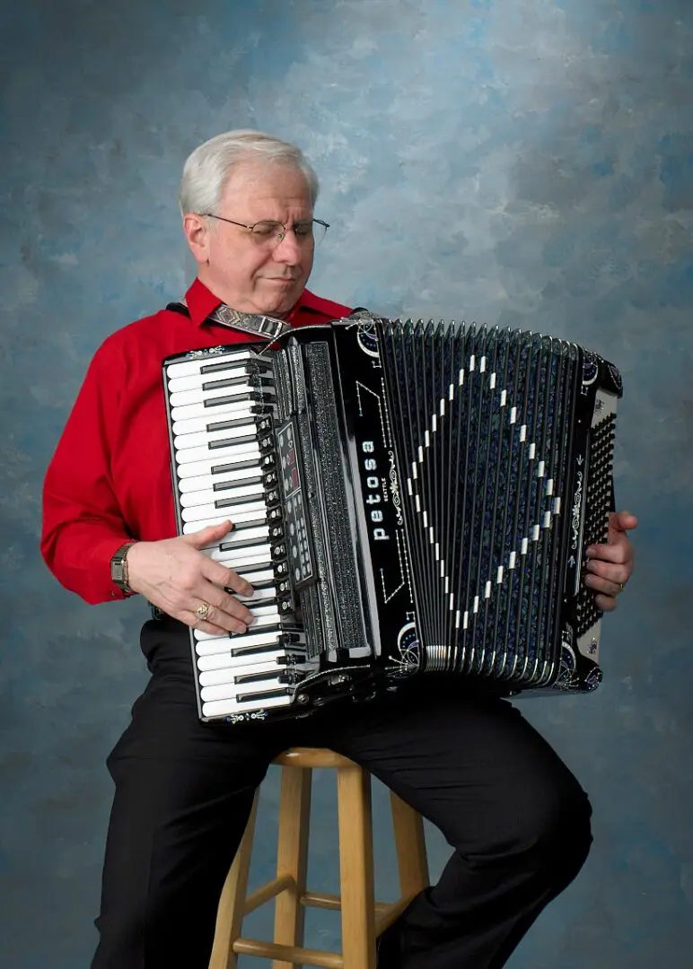 John Custie, a live musical entertainer, plays an accordion on a stool in Long Island, NY